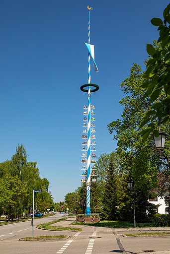 Traditioneller Maibaum in Aschheim Blau-weiß gestrichener Maibaum in Aschheim bei München mit Zunfttafeln und Kranz, umgeben von grünen Bäumen unter klarem, blauem Himmel.