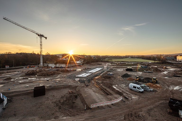 Großbaustelle bei Sonnenuntergang mit Kran und Baustellenfahrzeugen