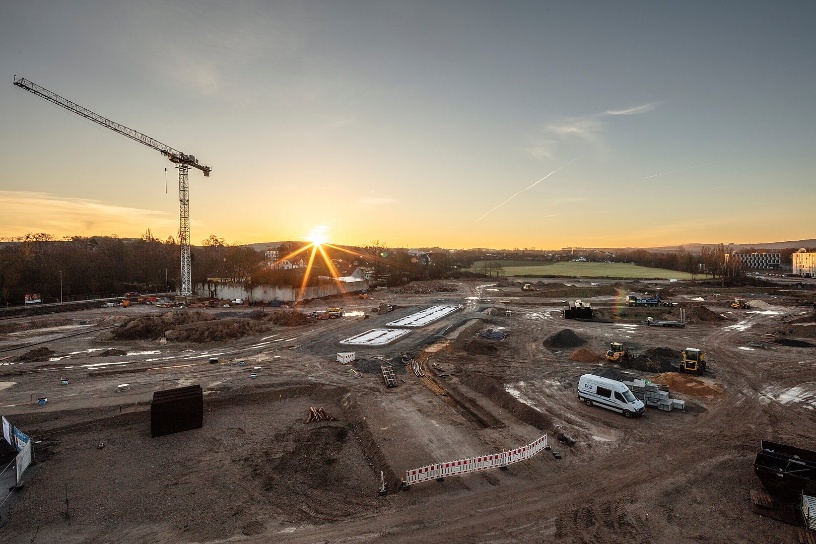 Großbaustelle bei Sonnenuntergang mit Kran und Baustellenfahrzeugen