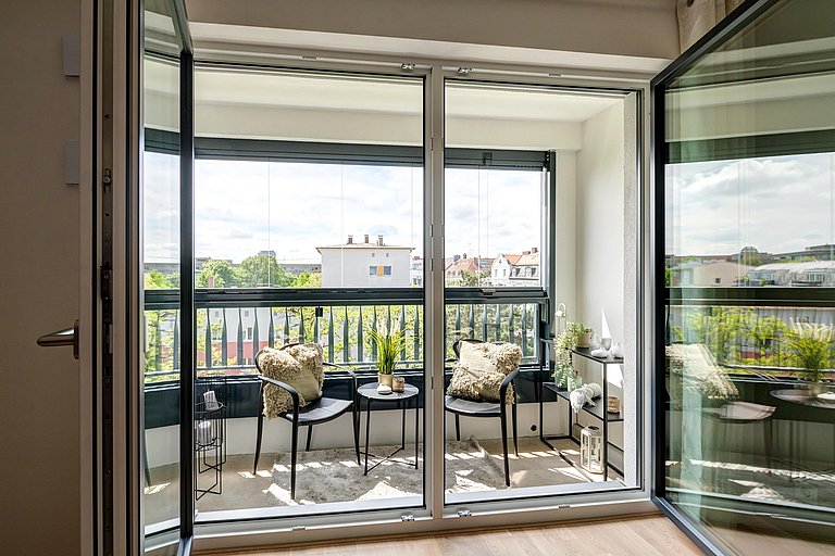 Gemütliche Loggia mit zwei Stühlen und kleinem Tisch mit Blick ins Grüne über die Dächer hinweg.