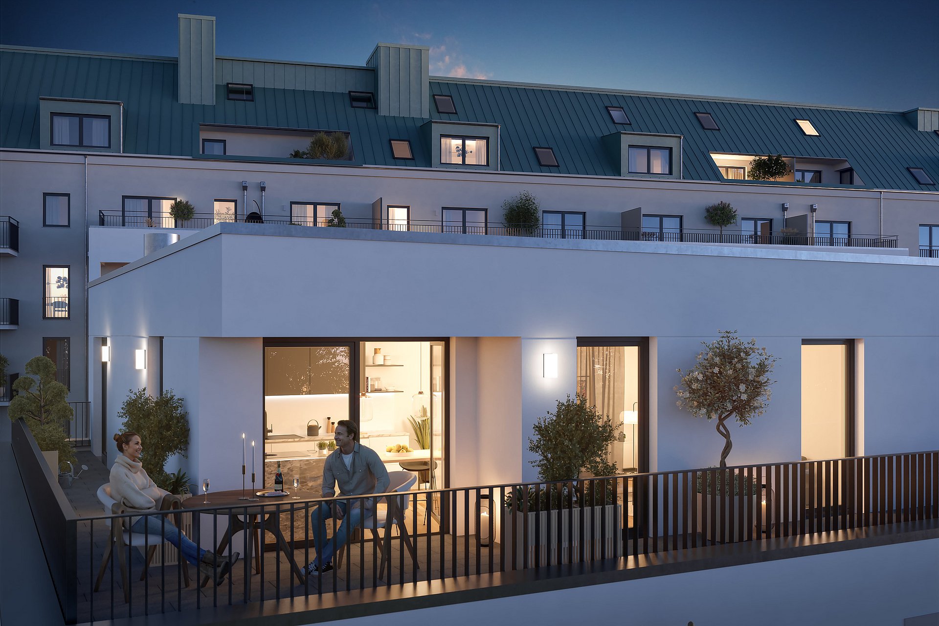Abendstimmung auf einem modernen Stadtbalkon: Zwei Personen sitzen entspannt bei Kerzenschein an einem Tisch, umgeben von stilvoller Bepflanzung, mit Blick auf die beleuchteten Wohnungen eines Mehrfamilienhauses mit grünem Dach.