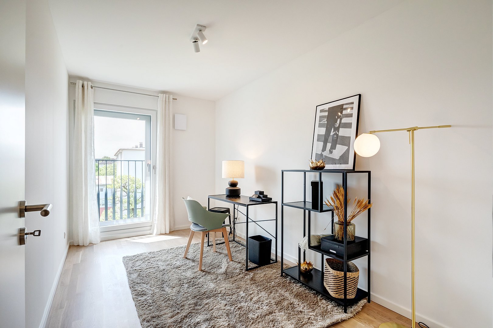 Helles Homeoffice mit Schreibtisch und minimalistischer Tischlampe, modernem Regal mit dekorativen Elementen, mit Zugang zum Balkon, gemütlichem Teppich und eleganter Stehlampe mit goldenem Gestell.