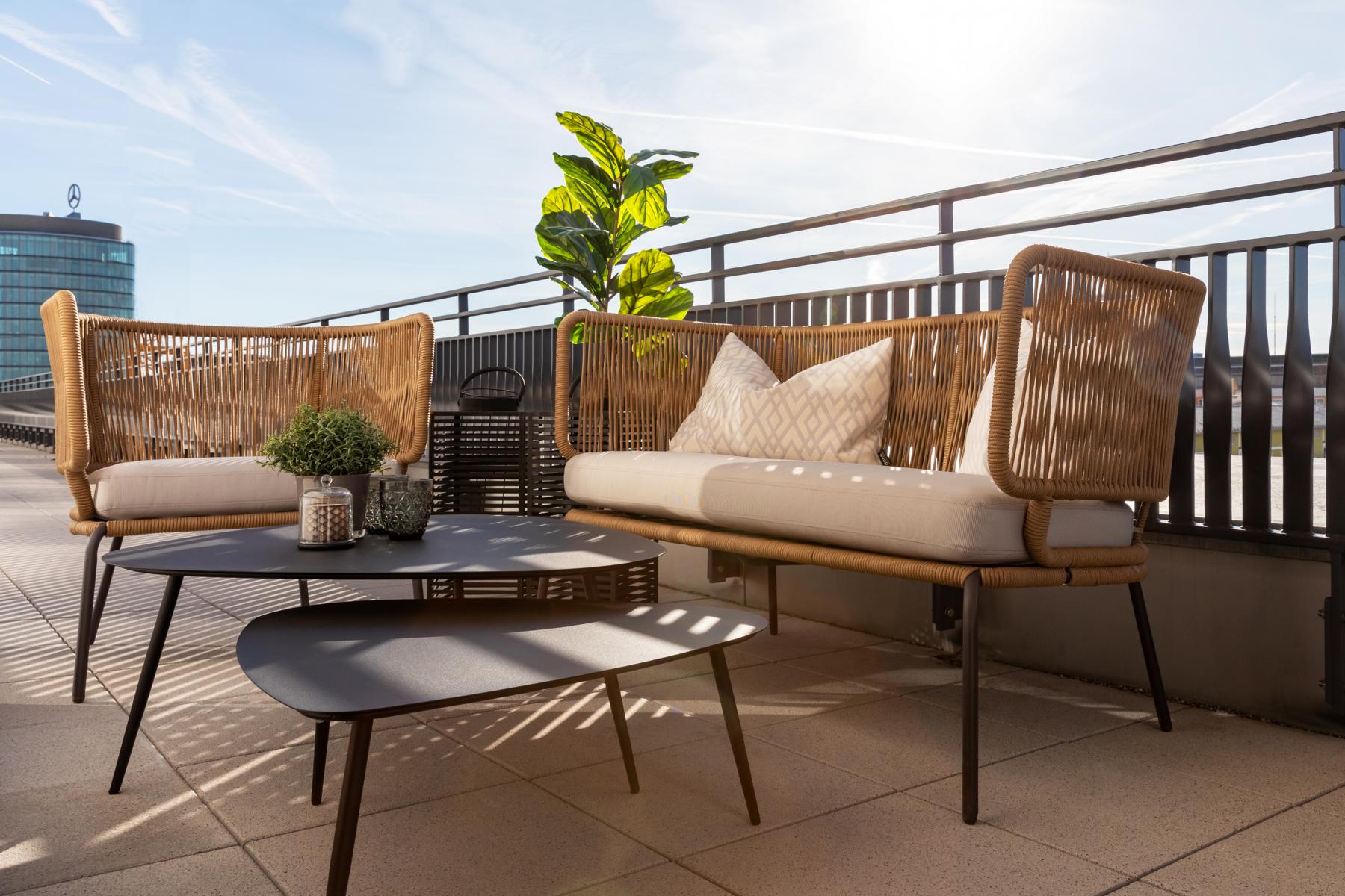 Dachterrasse mit gemütlichen Balkonmöbeln in Rattan-Optik mit passenden Sitzkissen und schwarzen Ablagetischen. 